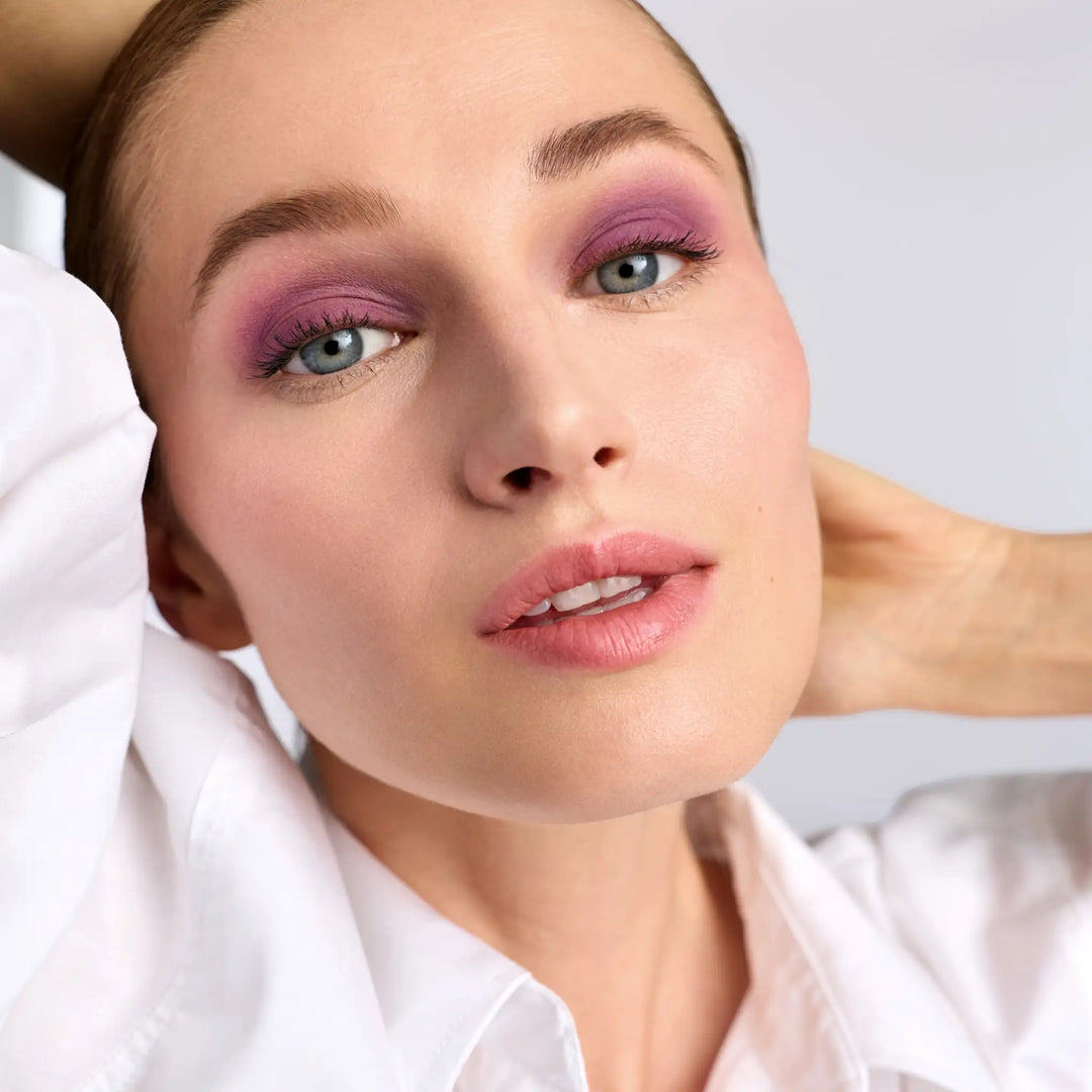 Model wearing Jane Iredale® ColorLuxe Eye Shadow Stick in Provence, a vibrant matte purple, paired with Jane Iredale® PureBronze Shimmer Bronzer in First Light, fresh radiant skin and a soft pink lip.