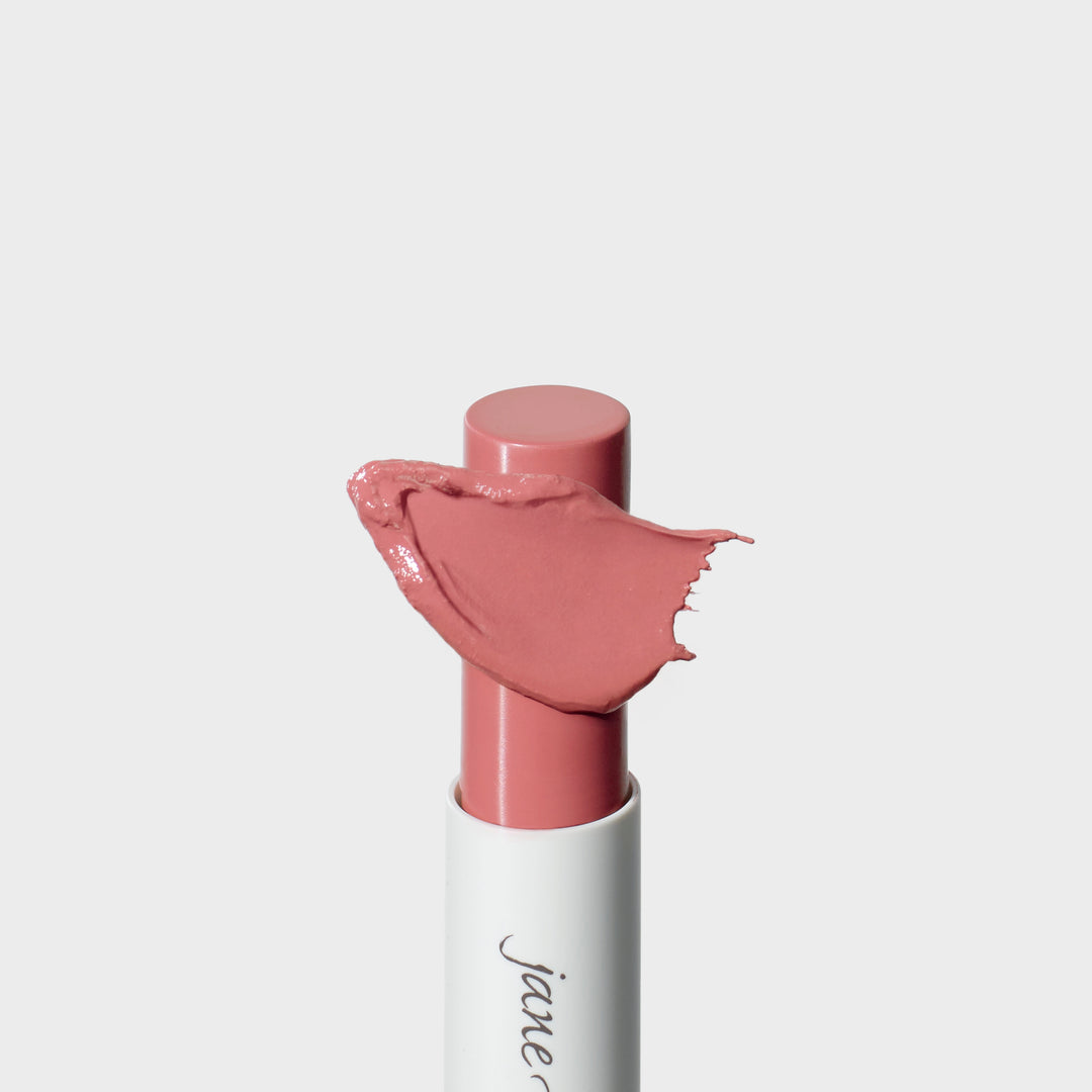 Jane Iredale® lipstick in Tutu, shown in a white tube with the lipstick bullet extended and a soft pink nude cream smear sweeping across the front.