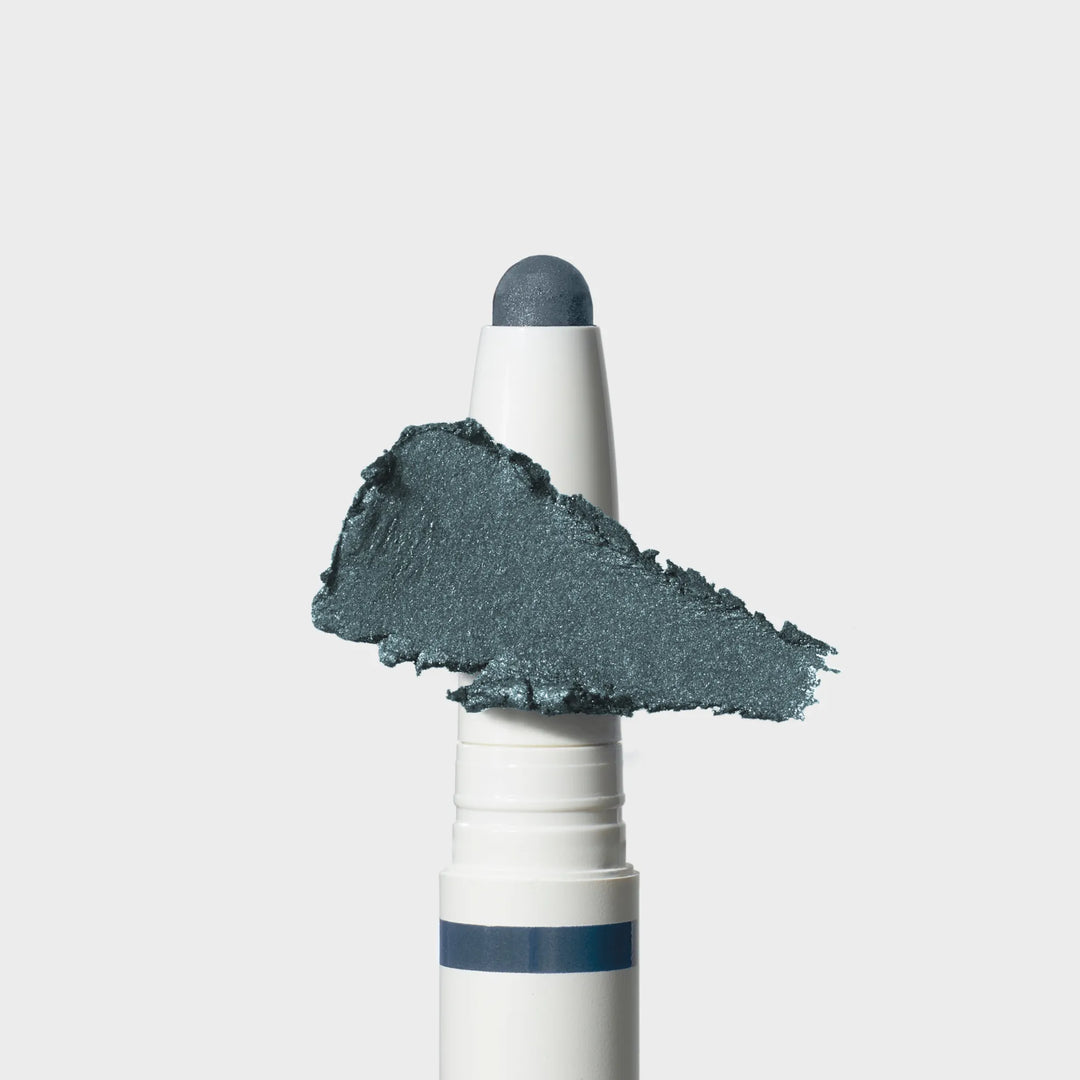 Jane Iredale® ColorLuxe Eye Shadow Stick in Riviera, shown in a white twist-up tube with the cream shadow bullet extended and a shimmering medium blue swipe across the front.