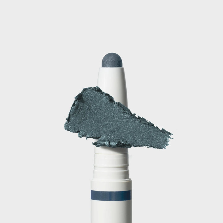 Jane Iredale® ColorLuxe Eye Shadow Stick in Riviera, shown in a white twist-up tube with the cream shadow bullet extended and a shimmering medium blue swipe across the front.